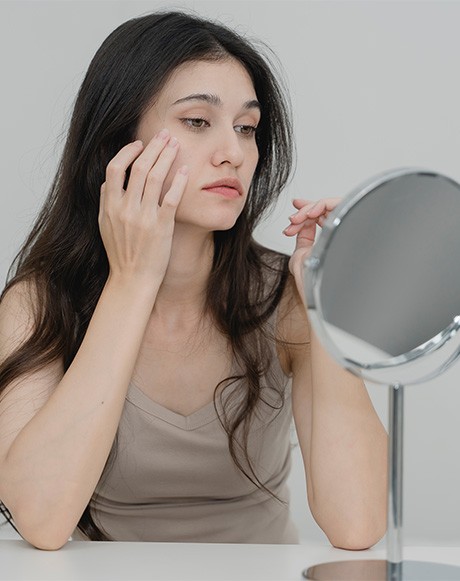 Woman looking at herself in mirror, concerned about signs of aging