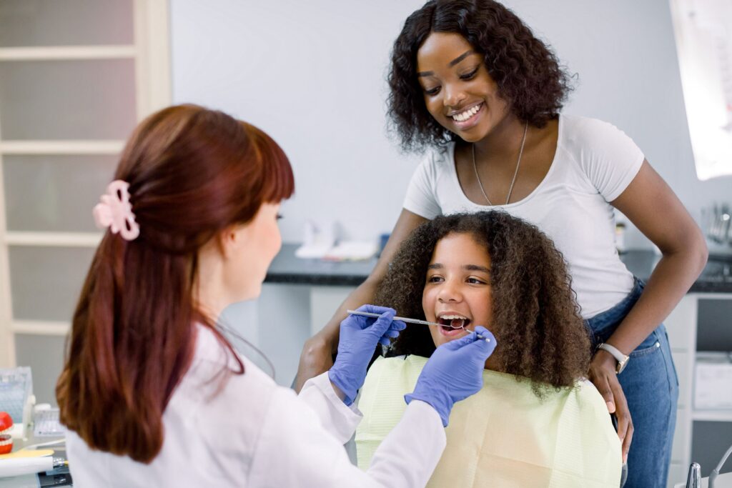 Mom standing behind girl in dental chair having teeth examined